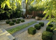 Ein Sitzplatz am Rande eines architektonisch gestalteten Hausgarten. Formgeschnittene Buchsbäume und strenge Linien outen den Garten klar als ein menschliches Kunstwerk.
